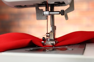 Photo of Sewing machine with red fabric indoors, closeup