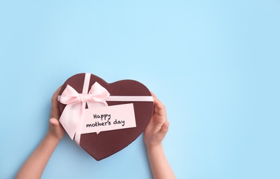 Child holding gift box for Mother's Day on color background