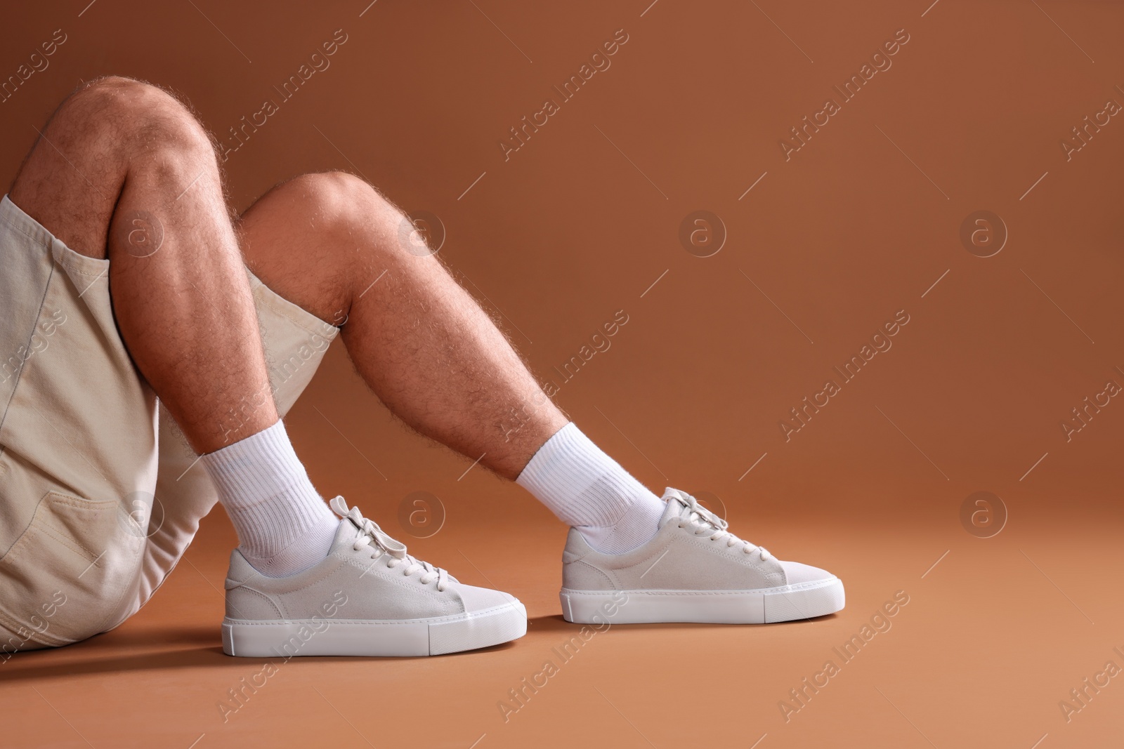 Photo of Man wearing stylish sneakers on brown background, closeup. Space for text