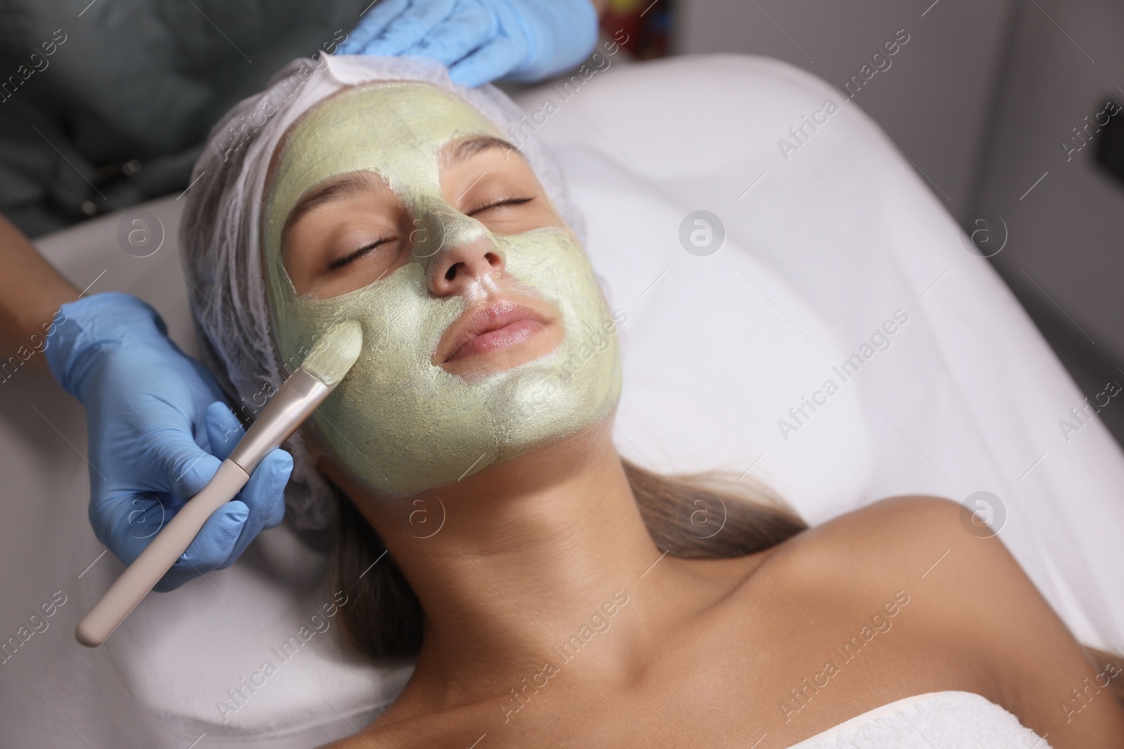 Photo of Cosmetologist applying mask on client's face in spa salon