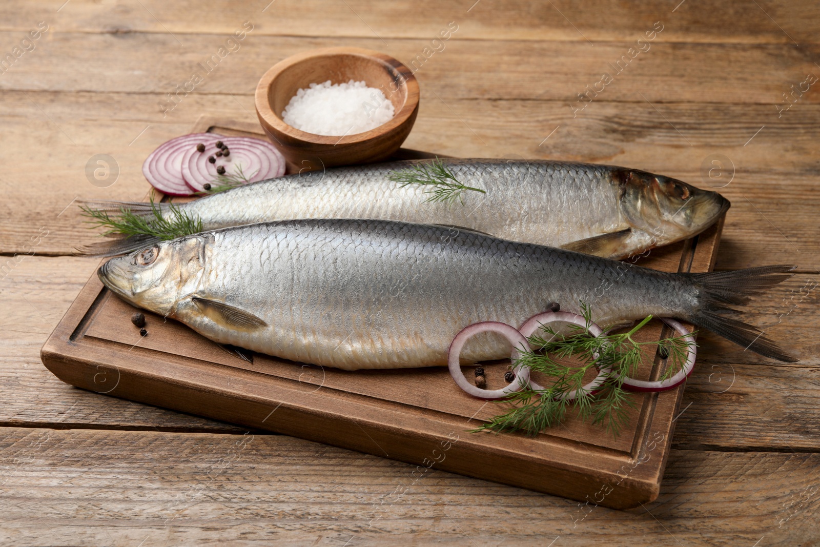 Photo of Board with delicious salted herrings, dill, onion and salt on wooden table