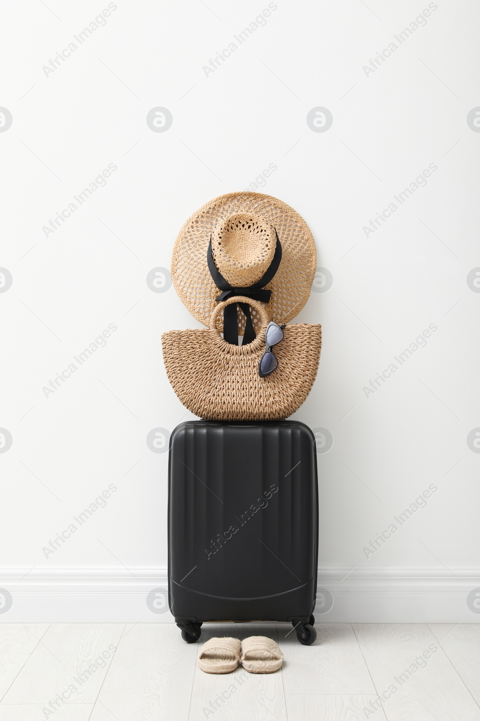 Photo of Suitcase packed for trip, shoes and summer accessories near white wall indoors