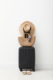Photo of Suitcase packed for trip, shoes and summer accessories near white wall indoors