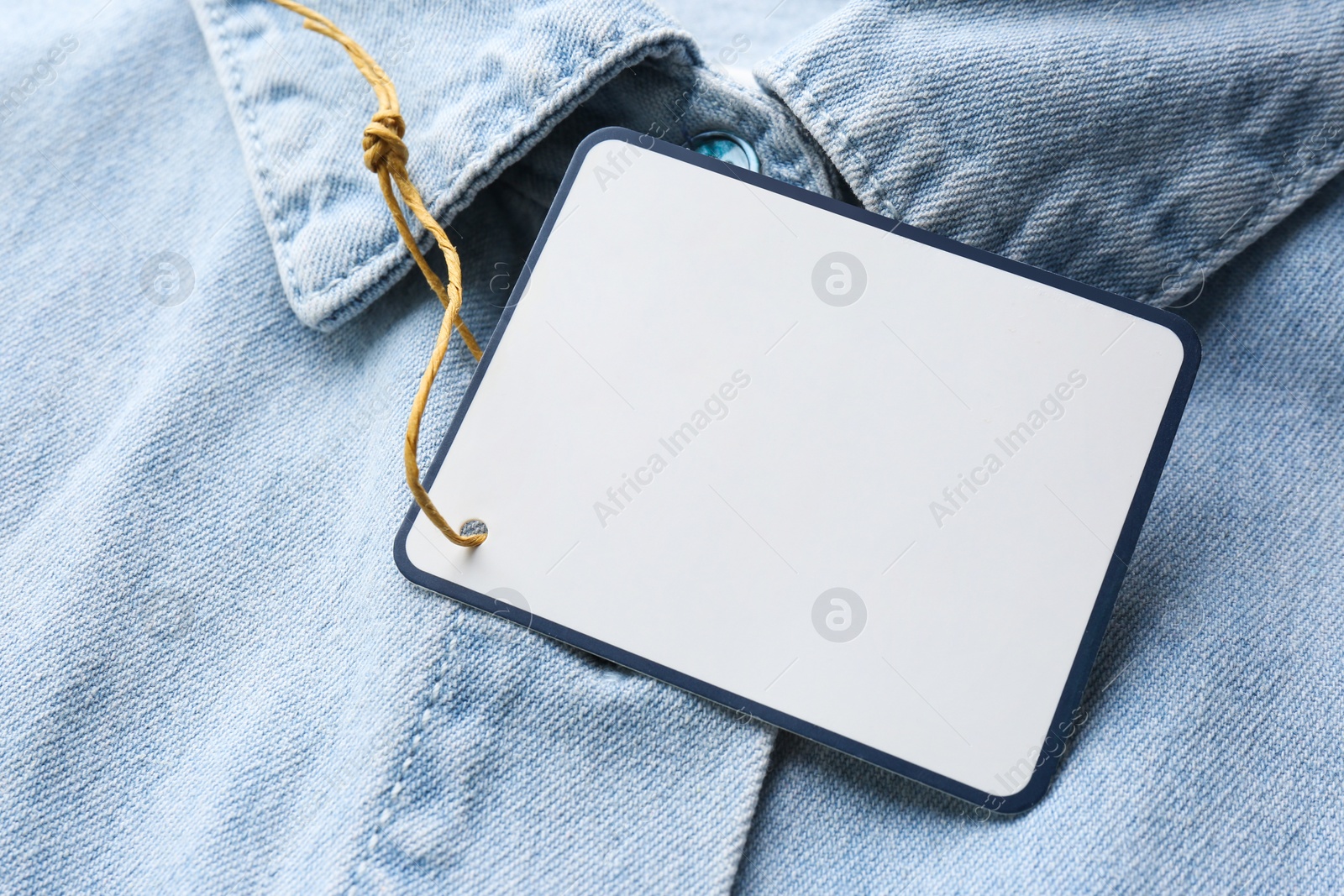 Photo of Blank tag on denim shirt, closeup view. Space for text