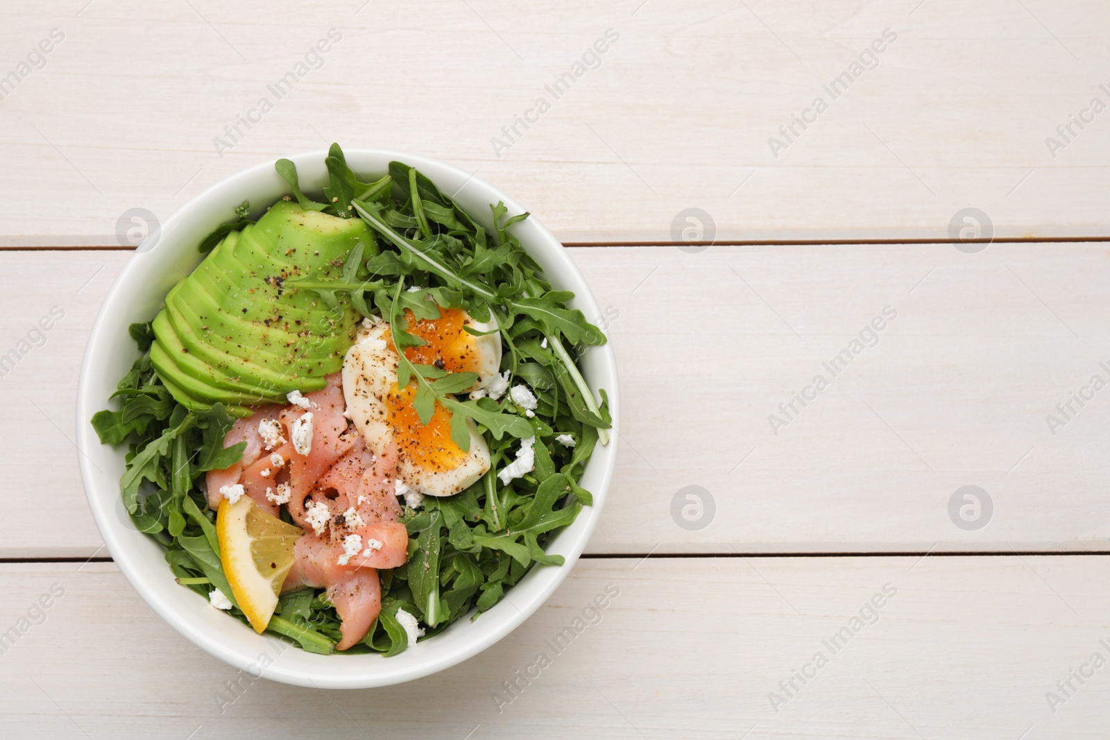 Photo of Delicious salad with boiled egg, salmon and avocado in bowl on white wooden table, top view. Space for text
