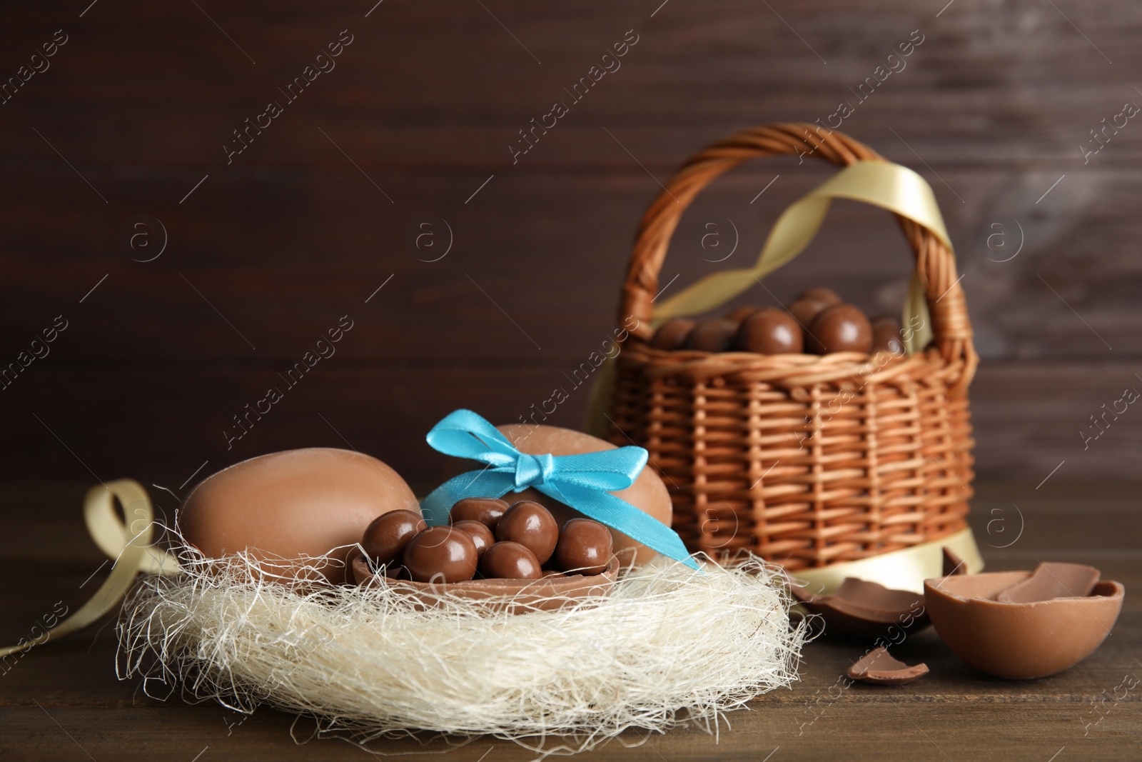 Photo of Tasty chocolate eggs with candies in decorative nest on wooden table