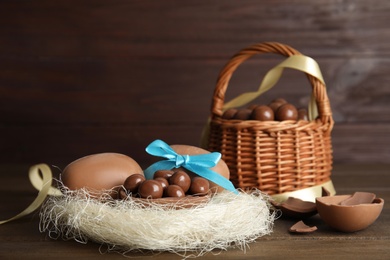 Photo of Tasty chocolate eggs with candies in decorative nest on wooden table