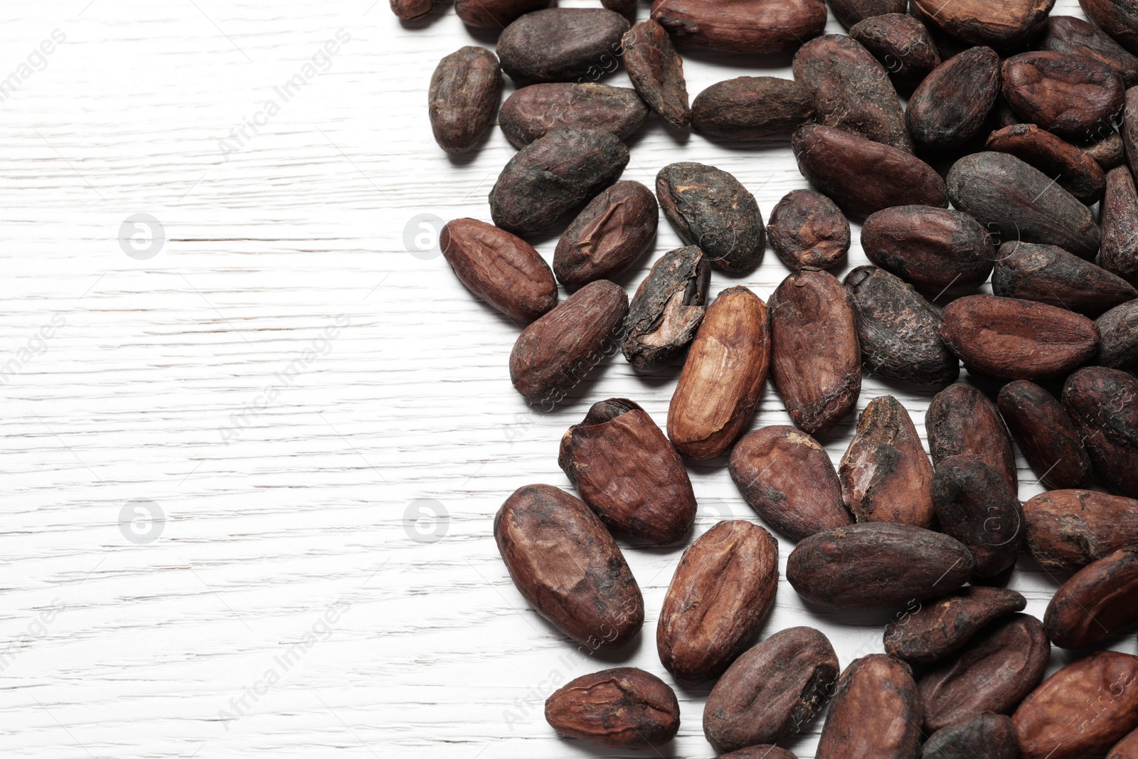 Photo of Tasty cocoa beans on white wooden table, above view. Space for text