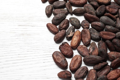 Photo of Tasty cocoa beans on white wooden table, above view. Space for text