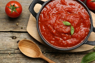 Photo of Homemade tomato sauce in bowl, spoon and fresh ingredients on wooden table, flat lay
