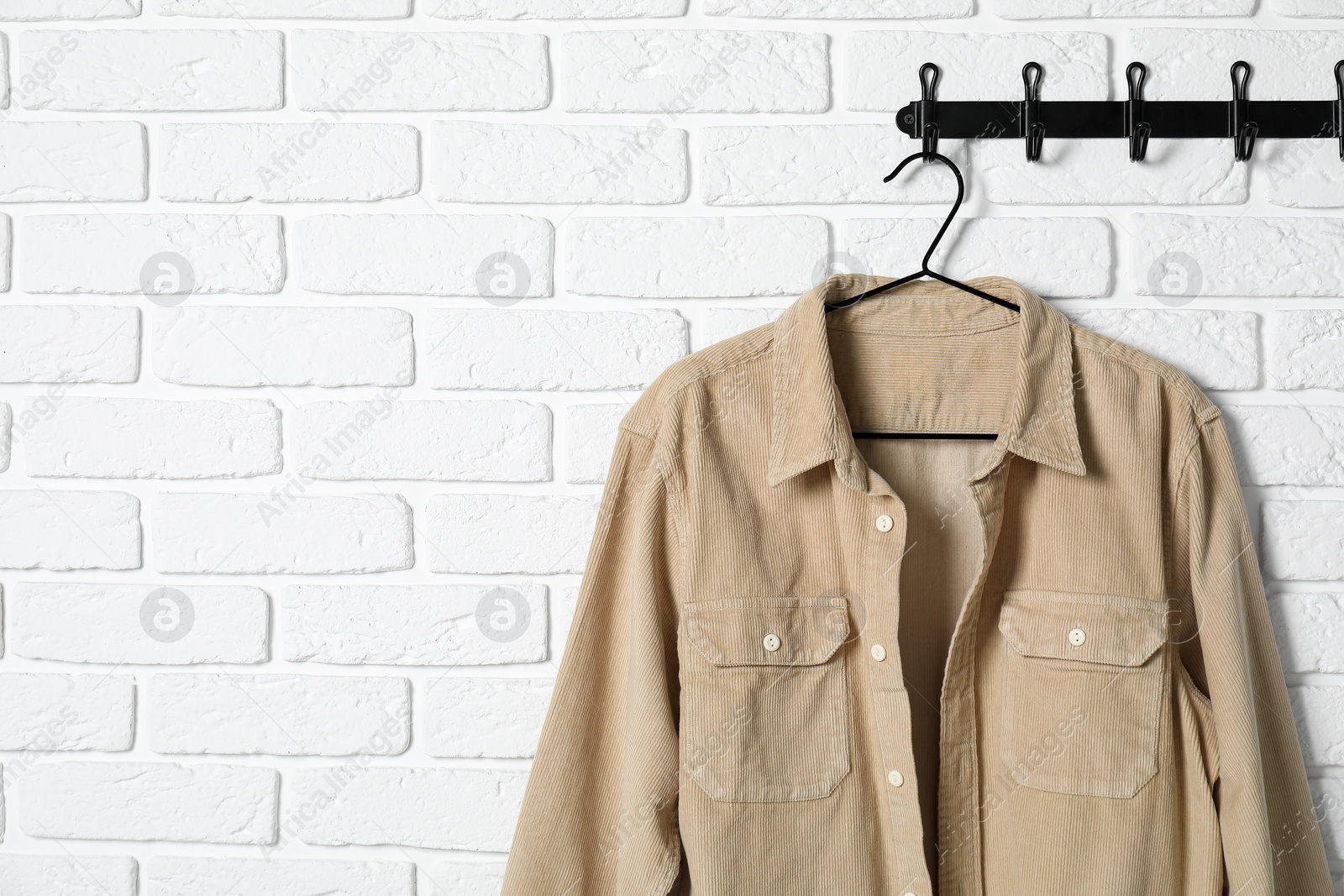 Photo of Hanger with beige shirt on white brick wall, space for text
