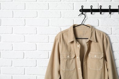 Hanger with beige shirt on white brick wall, space for text