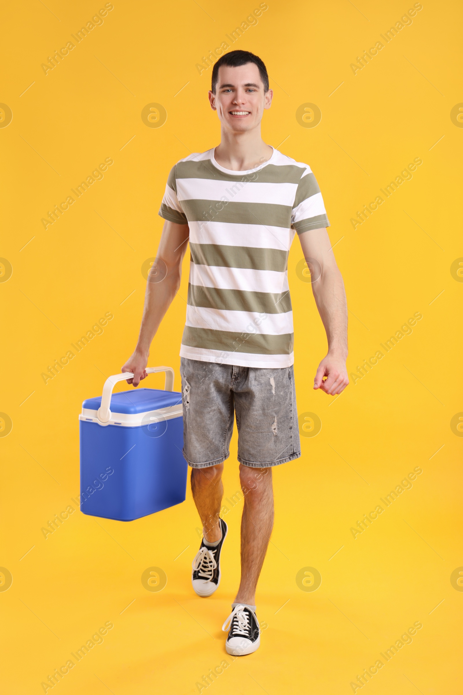 Photo of Man with blue cool box walking on orange background