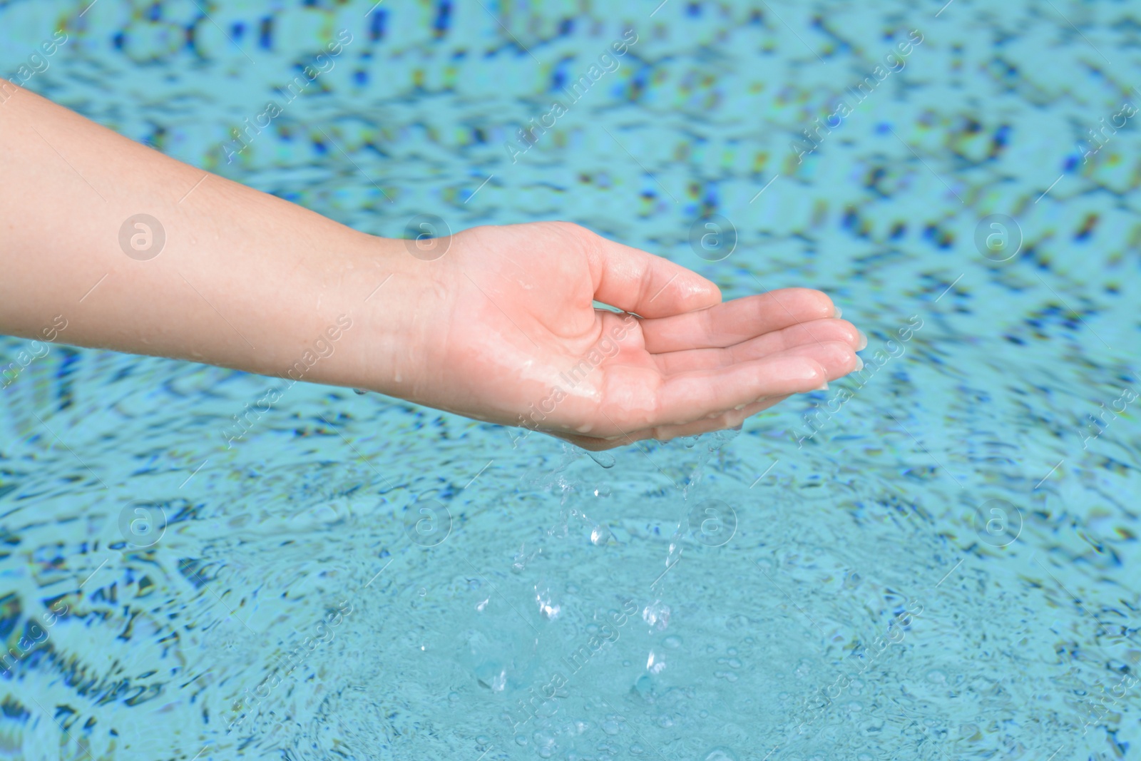 Photo of Girl holding water in hand above pool, closeup