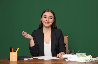 Portrait of young teacher at table against green background