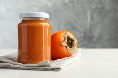 Delicious persimmon jam in glass jar and fresh fruit on white wooden table, space for text