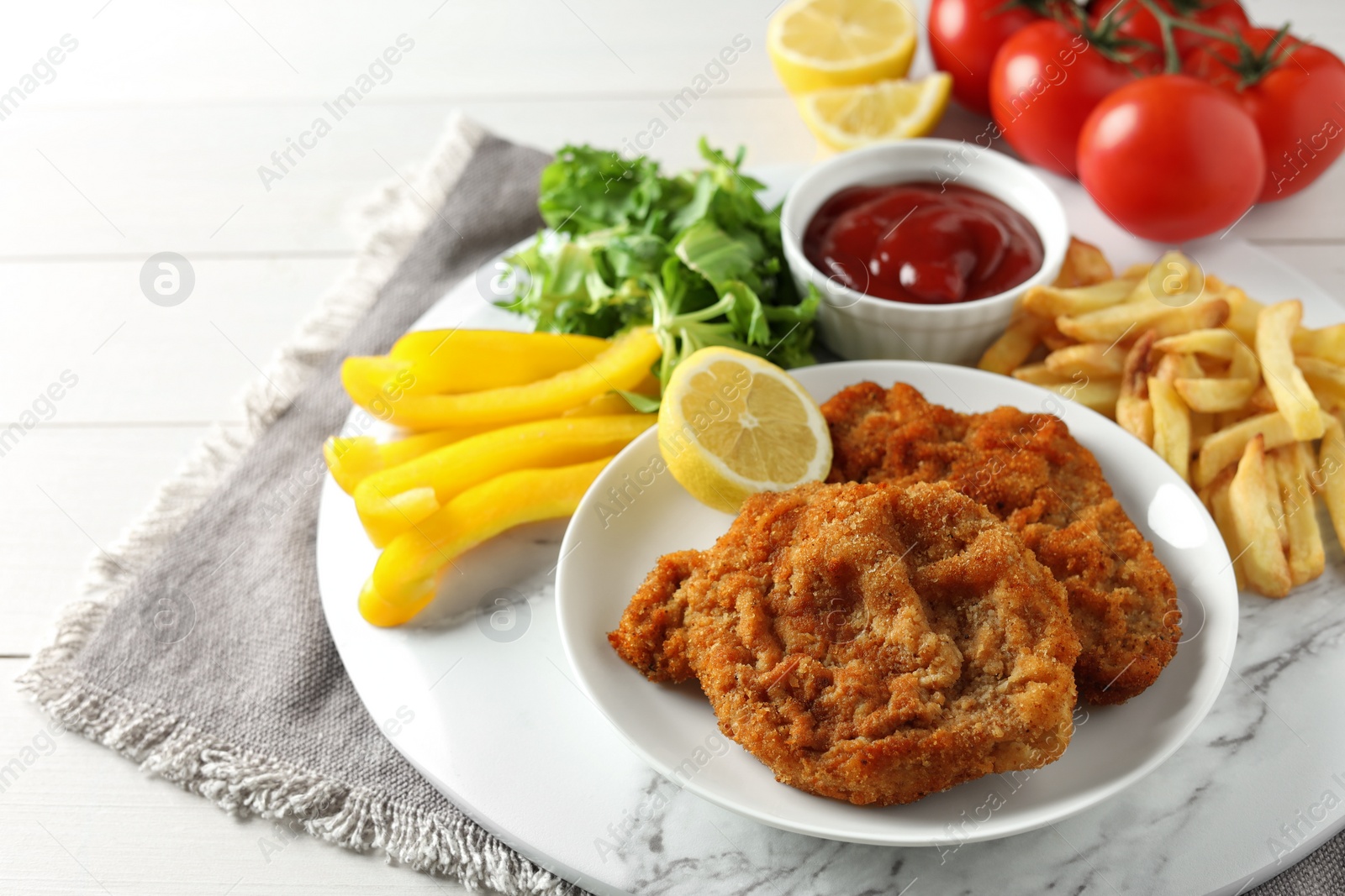 Photo of Tasty schnitzels served with potato fries, ketchup and vegetables on white wooden table, closeup
