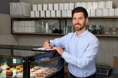 Photo of Happy business owner with clipboard and pen in bakery shop
