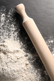 Photo of Pile of flour and rolling pin on black textured table, top view