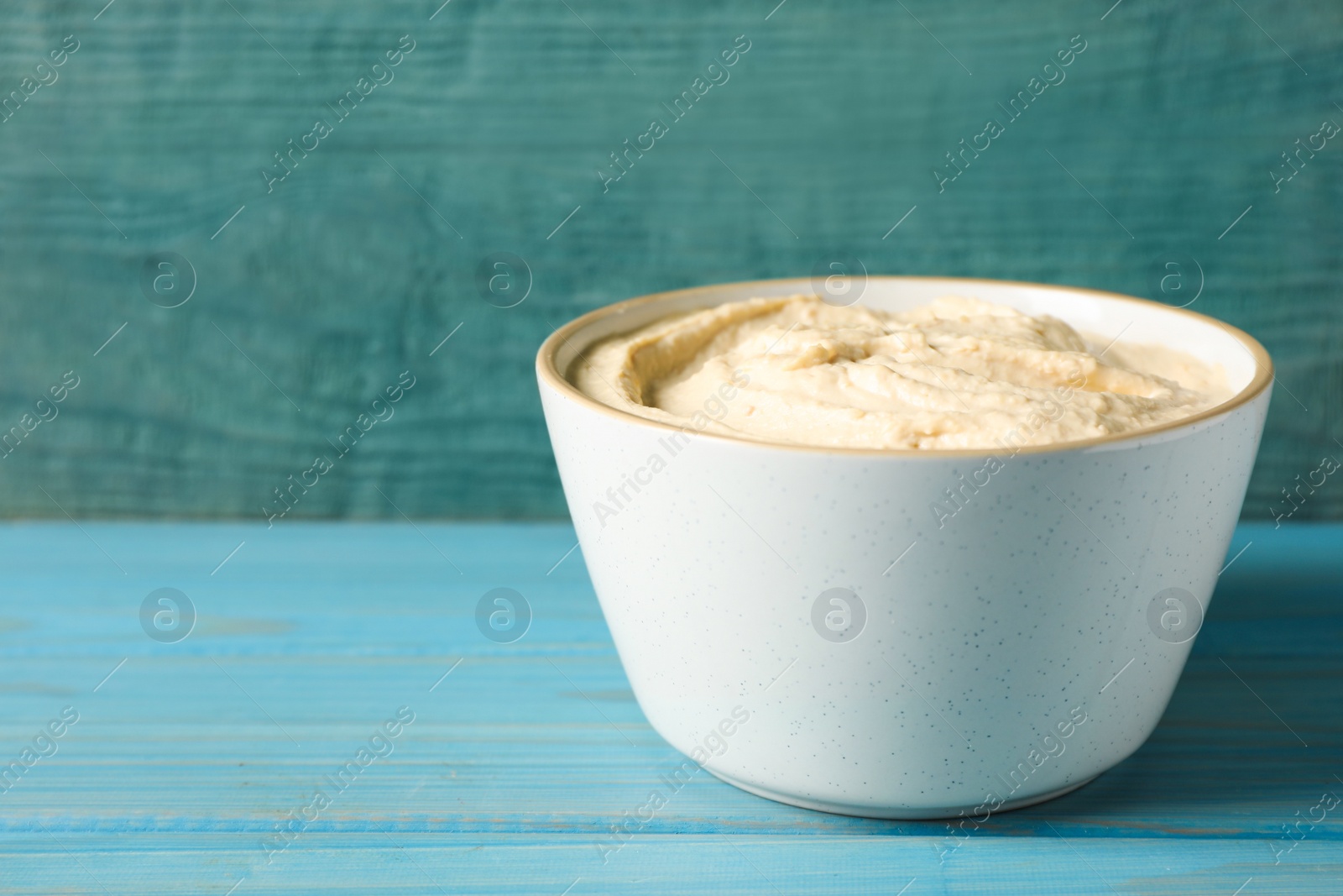 Tasty hummus in bowl on light blue table against wooden background. Space for text Photo of Tasty hummus in bowl on light blue table against wooden background. Space for text