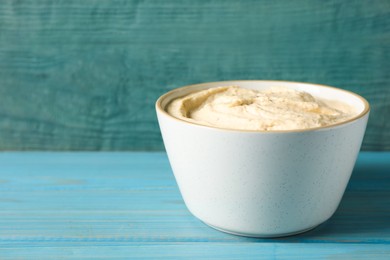 Photo of Tasty hummus in bowl on light blue table against wooden background. Space for text