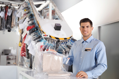 Photo of Portrait of happy worker with clothes near counter at dry-cleaner's