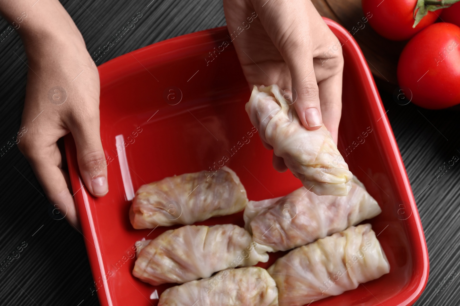 Photo of Woman putting uncooked stuffed cabbage roll into baking dish at black table, top view