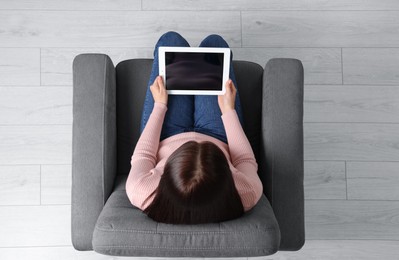 Woman working with tablet in armchair, top view