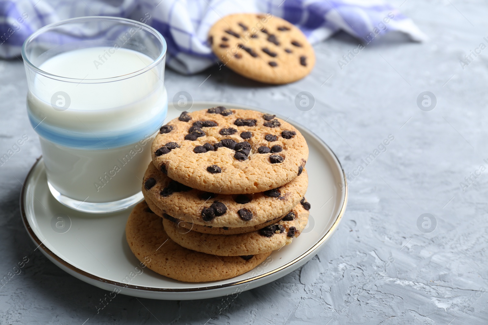 Photo of Delicious chocolate chip cookies and glass of milk on grey textured table, space for text