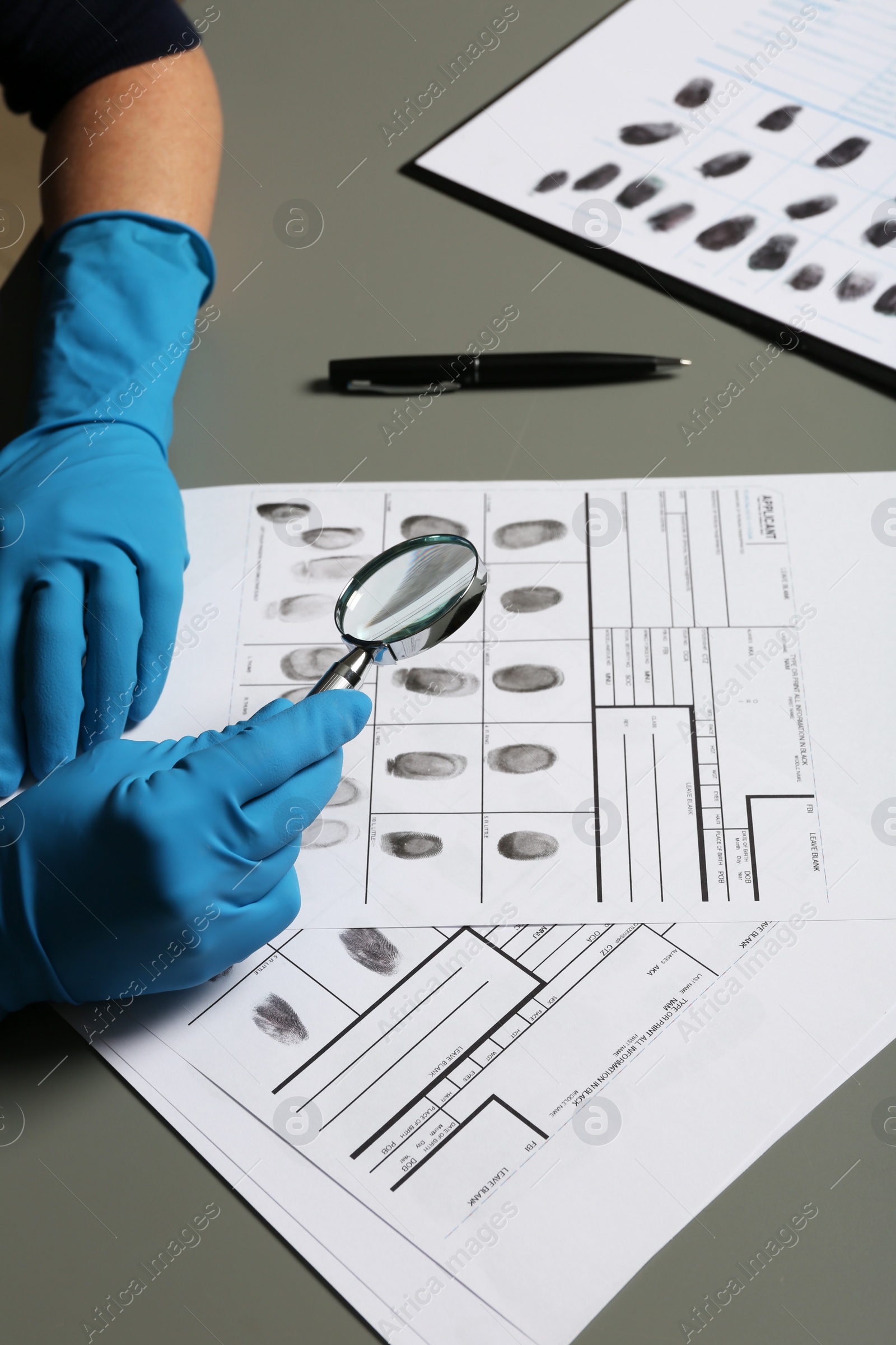 Photo of Criminalist exploring fingerprints with magnifying glass at table, closeup