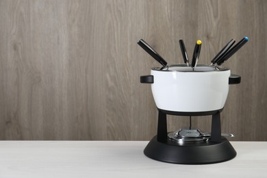 Photo of Fondue set on white wooden table, space for text