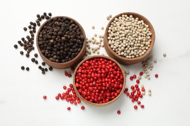 Aromatic spice. Different peppers in bowls on white table, flat lay