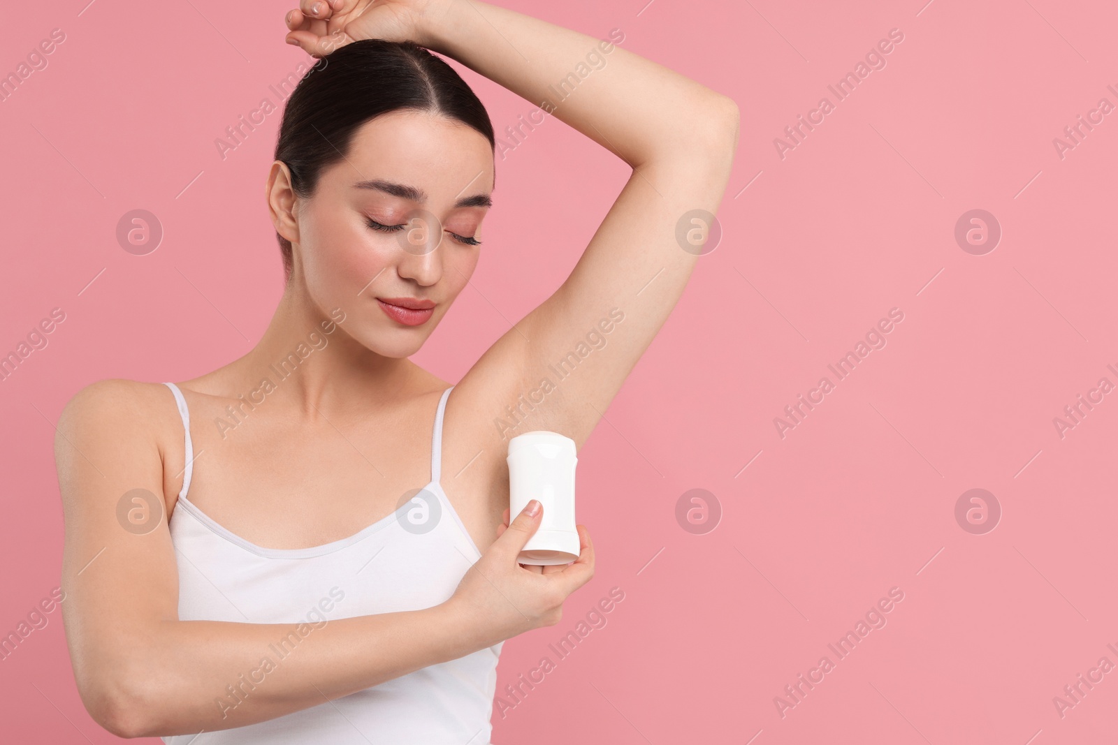 Photo of Beautiful woman applying deodorant on pink background, space for text