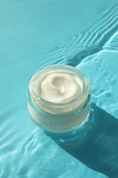 Photo of Jar with moisturizing cream in water on light blue background