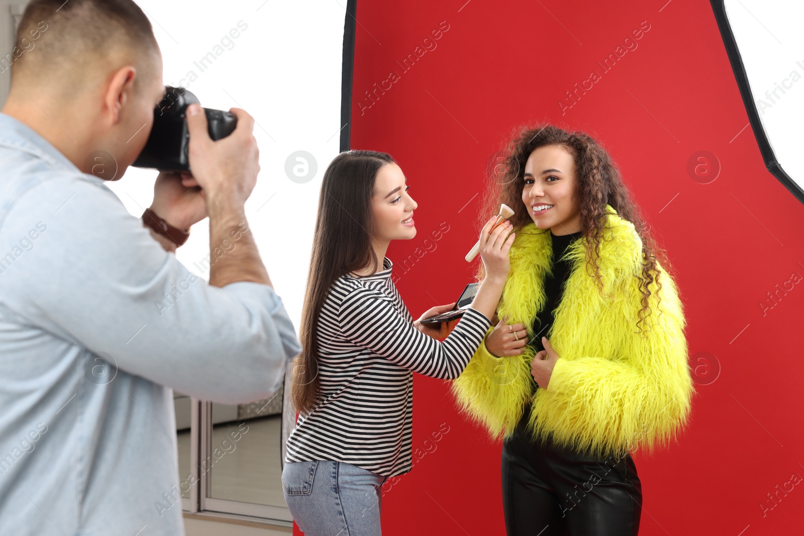 Photo of Professional photographer and makeup artist with model in studio