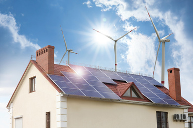 Wind turbines near house with installed solar panels on roof. Alternative energy source