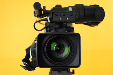 Photo of Modern professional video camera on yellow background, closeup