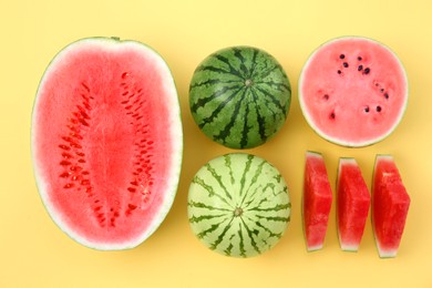 Different cut and whole ripe watermelons on yellow background, flat lay