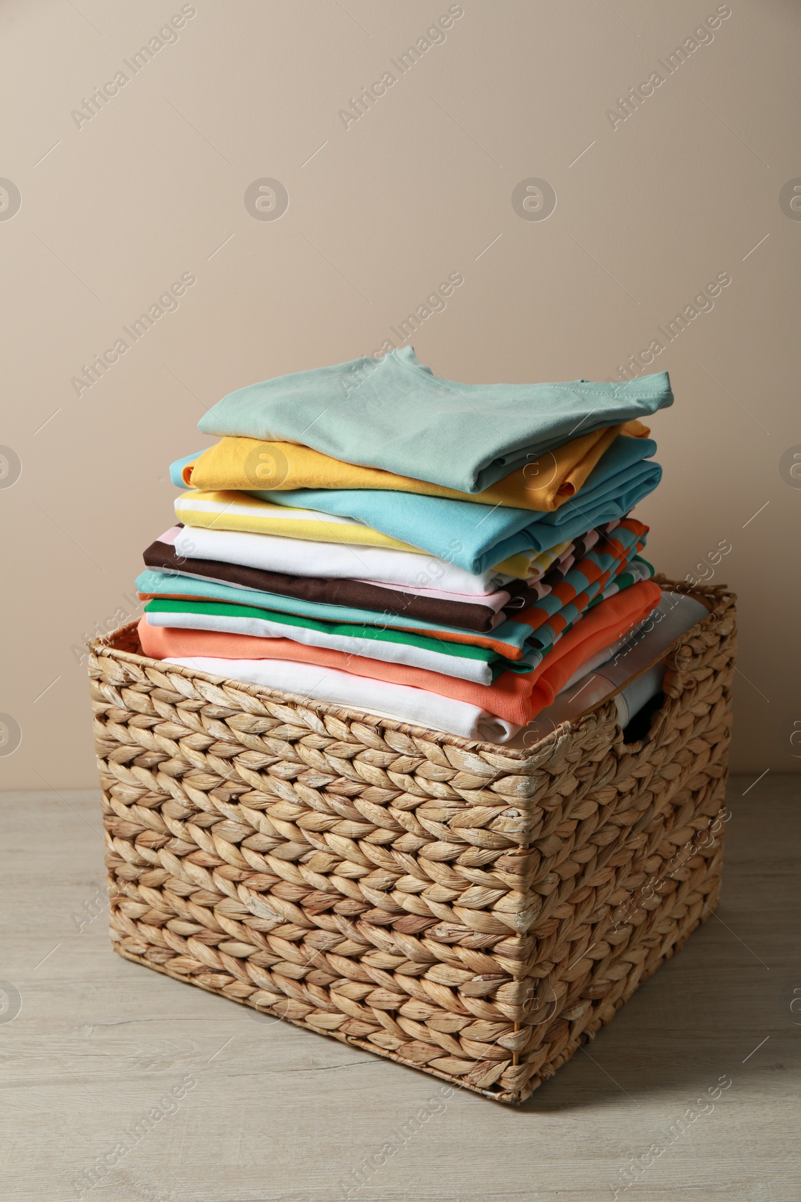 Photo of Wicker laundry basket with clean clothes on floor near beige wall