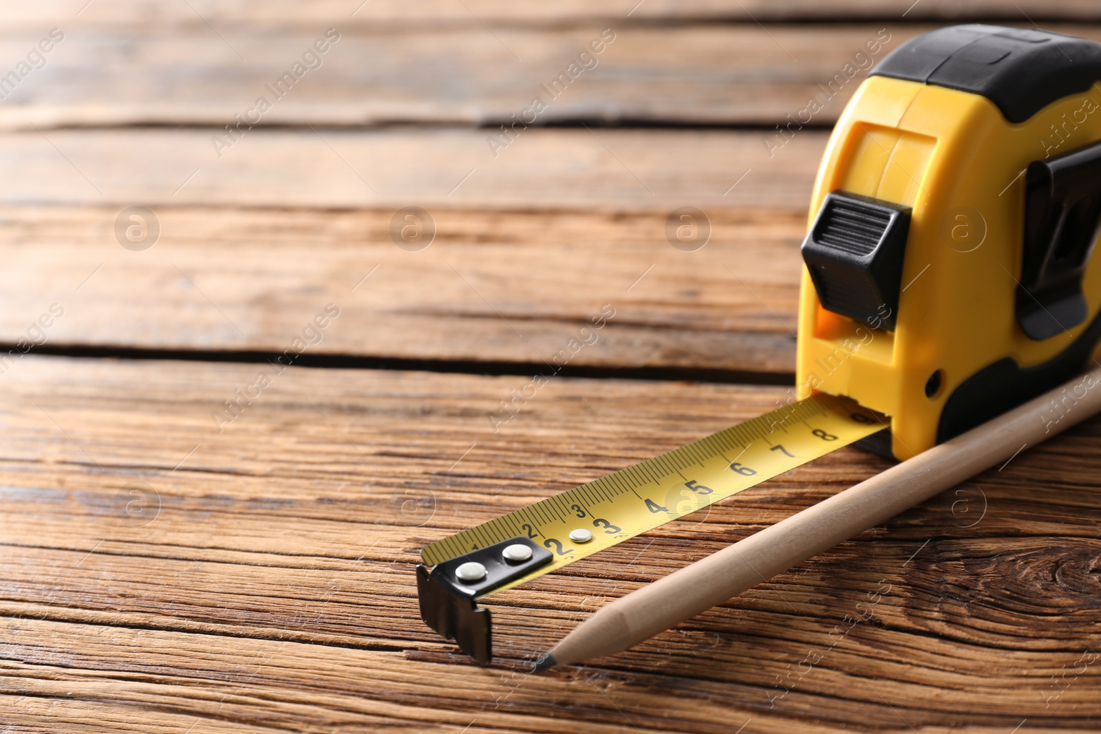 Photo of Metal measuring tape and pencil on wooden background. Space for text