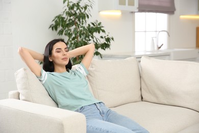 Young woman relaxing on sofa at home, space for text