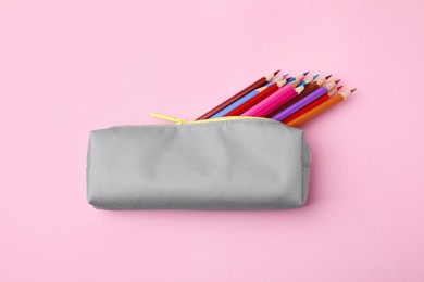 Photo of Many colorful pencils in pencil case on pink background, top view