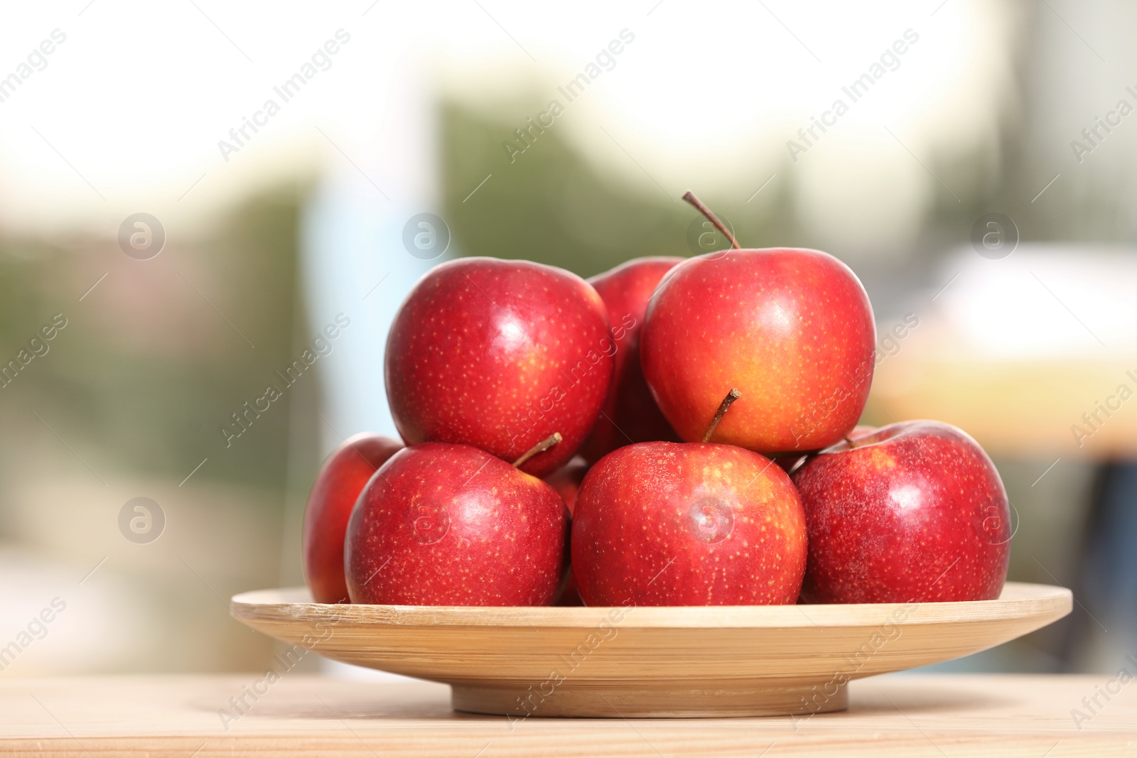 Photo of Plate with sweet red apples on table against blurred background, closeup