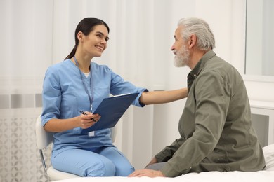 Photo of Smiling nurse with clipboard supporting elderly patient in hospital