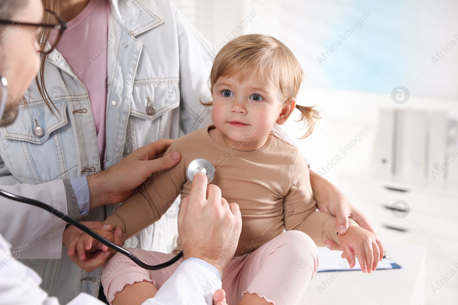 Photo of Mother and her cute baby having appointment with pediatrician in clinic. Doctor examining little girl