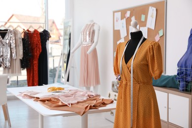 Photo of Mannequin with stylish orange dress and measuring tape in atelier