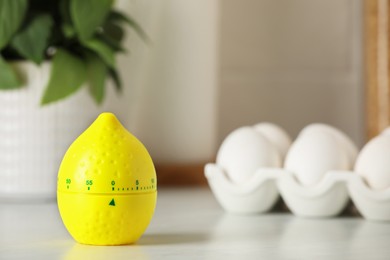 Kitchen timer in shape of lemon and eggs on white table. Space for text
