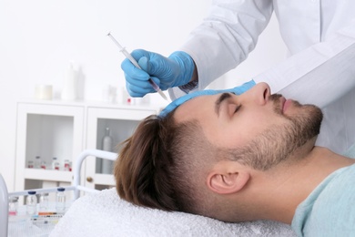 Photo of Young man with hair loss problem receiving injection in salon