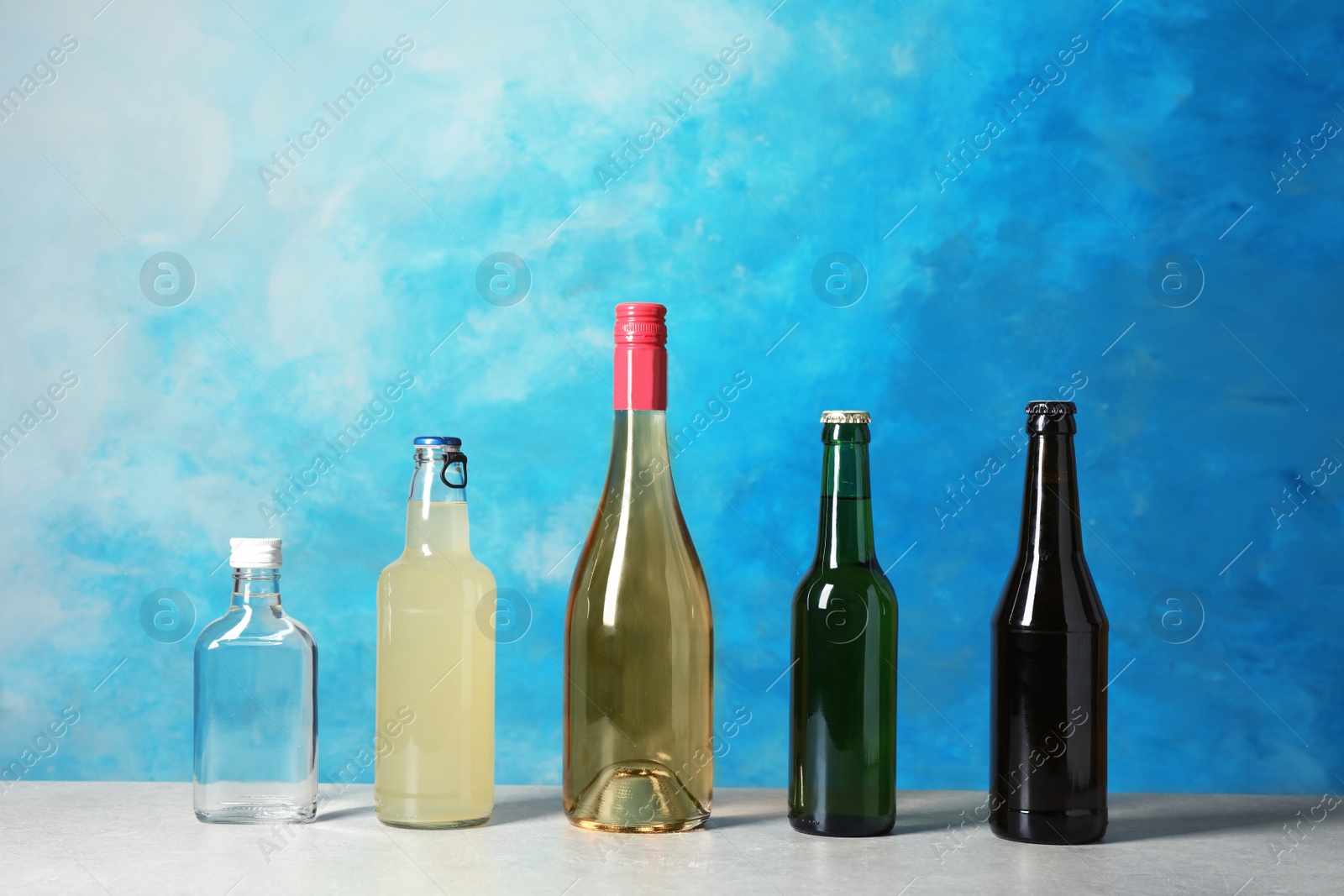 Photo of Bottles with different alcoholic drinks on table against color background