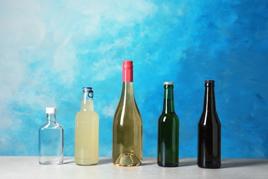 Photo of Bottles with different alcoholic drinks on table against color background